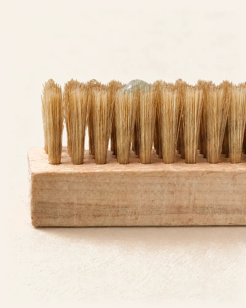 A drop of CAFFREY cleaner resting on the tan bristle tips of the kit’s wooden brush