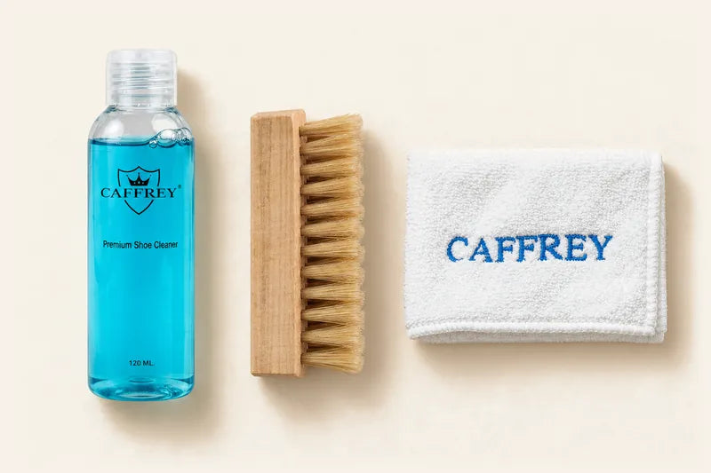 CAFFREY shoe cleaner bottle, wooden brush with tan bristles and white embroidered cloth laid side by side