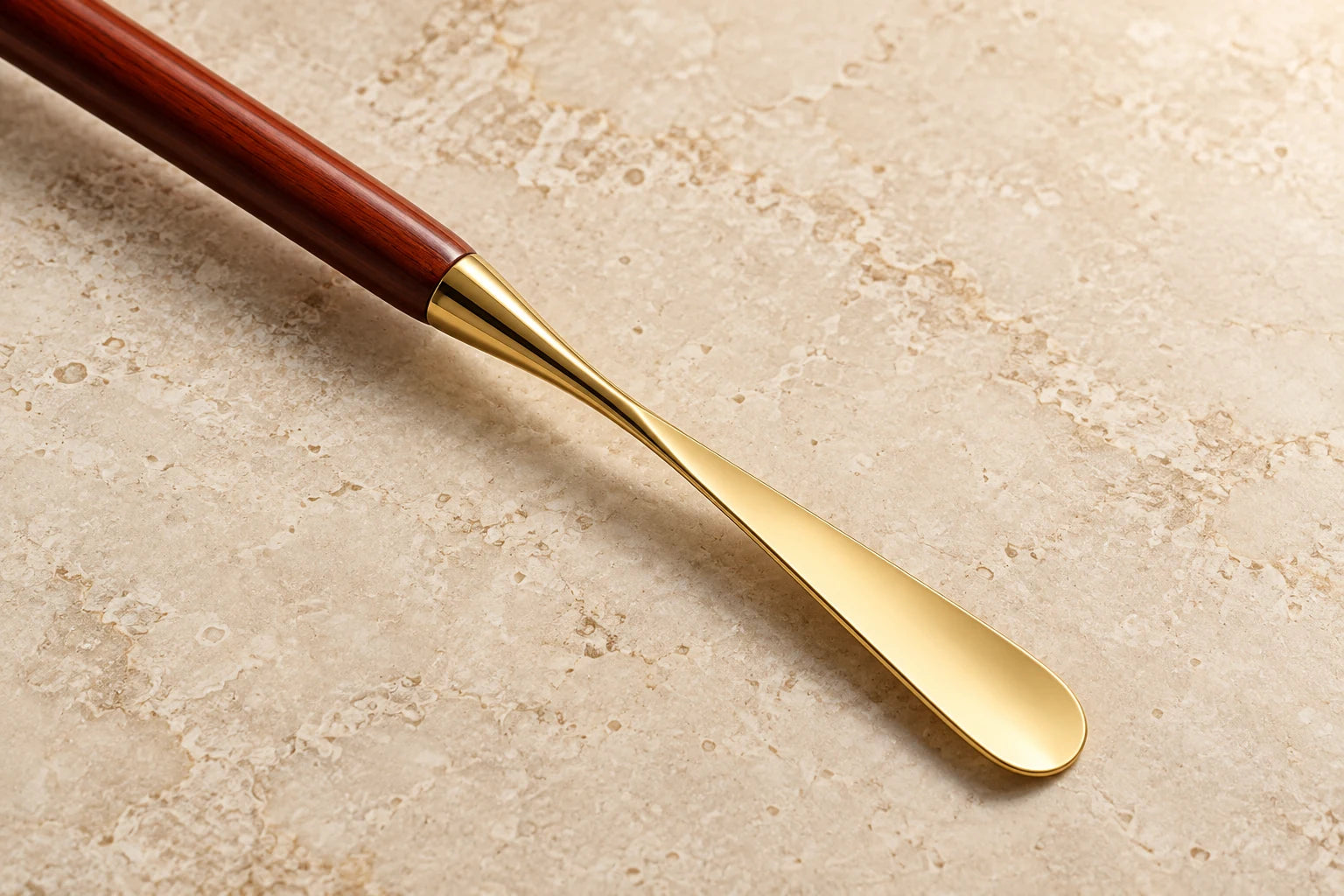 Close-up of the polished wood shaft meeting the curved gold-tone shoehorn blade on ivory stone