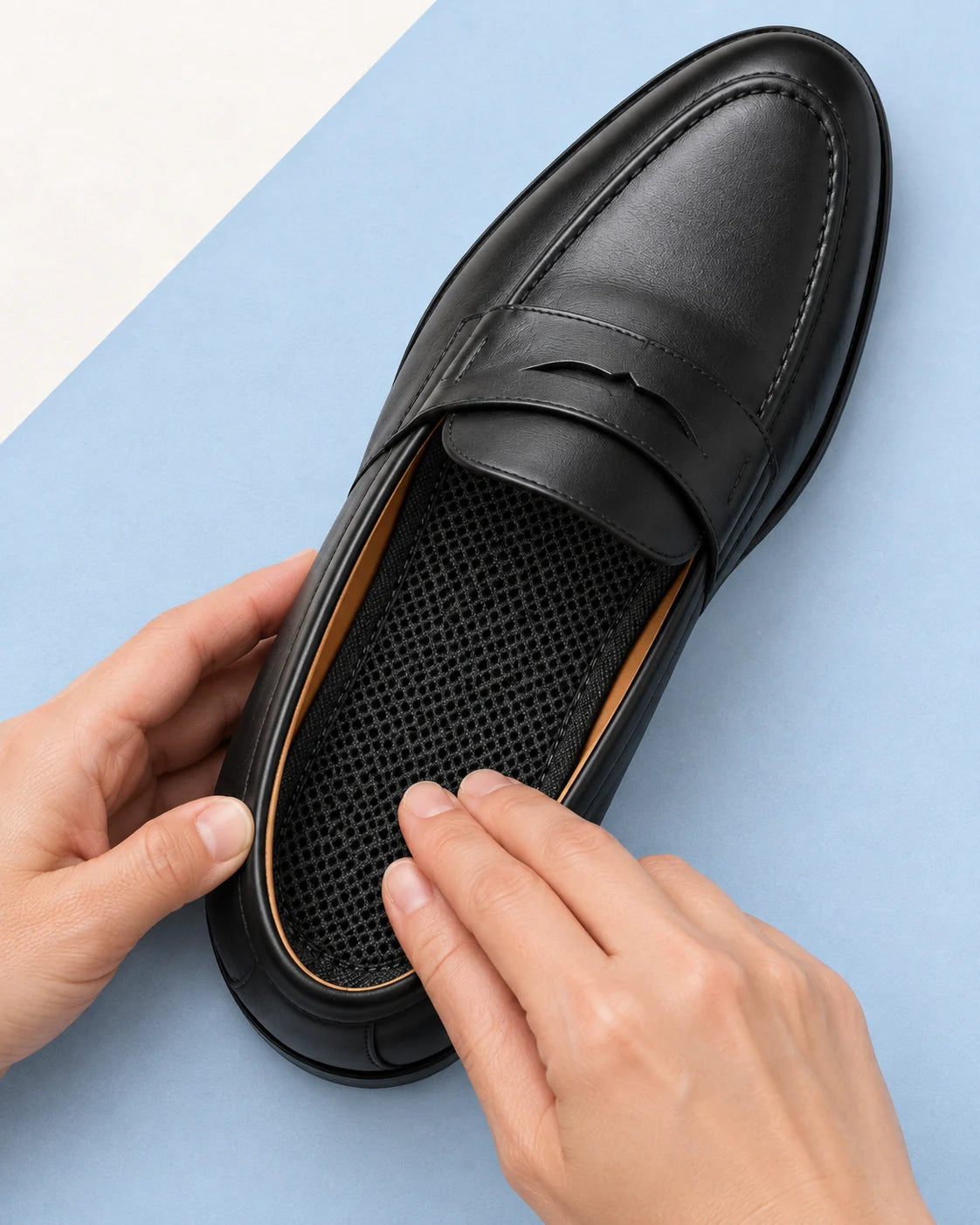 Hands pressing the Zephyr mesh heel flat inside the same black penny loafer, with mesh facing up