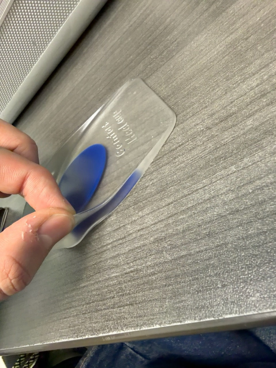 A hand lifting the flexible clear edge of the blue gel heel pad from a tabletop