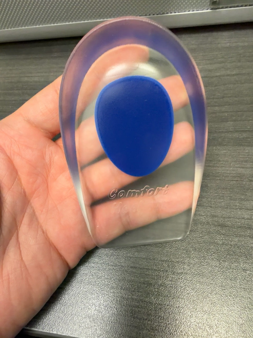 Blue Men CAFFREY Gel Heel Pad held in a hand, showing its clear gel body and Comfort Heel Cup marking