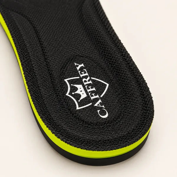 Close-up of the heel of a Comfort Max insole: black fabric top with the white CAFFREY crest, over a lime side wall