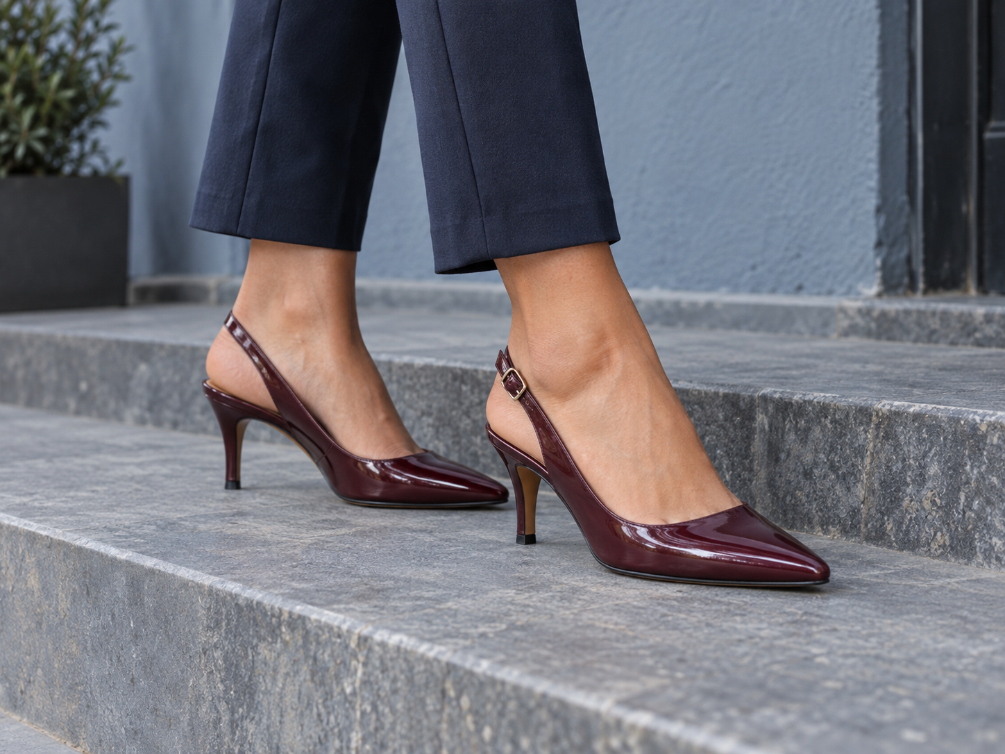 Burgundy slingback pumps worn with navy trousers on grey stone steps