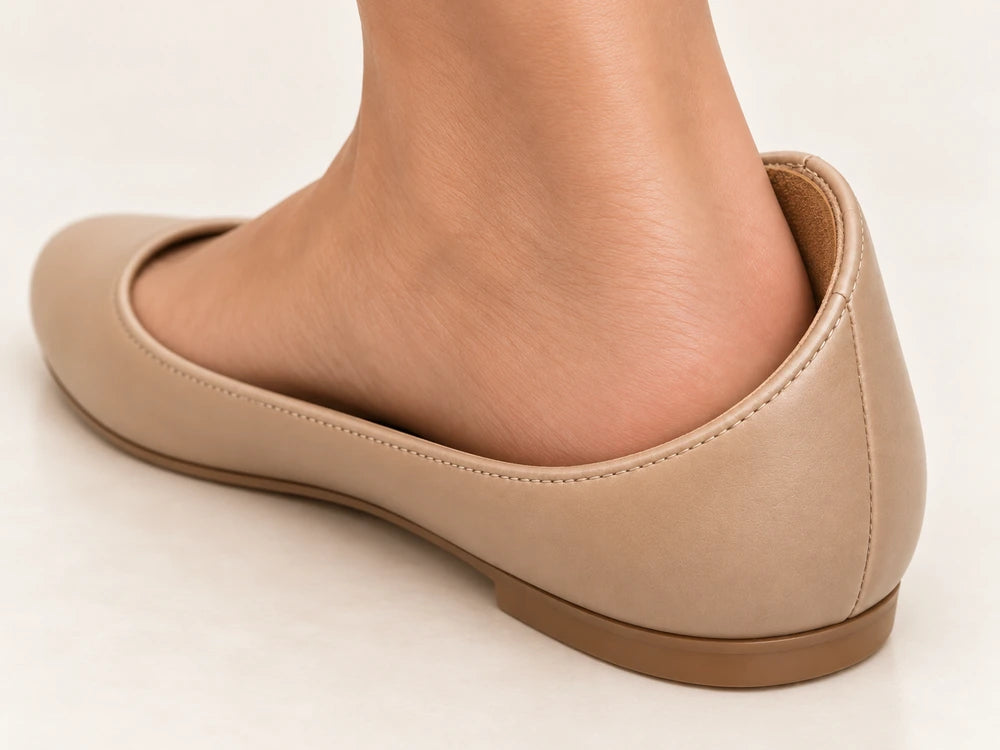 A woman wearing a beige shoe with a brown heel grip fitted inside against her heel