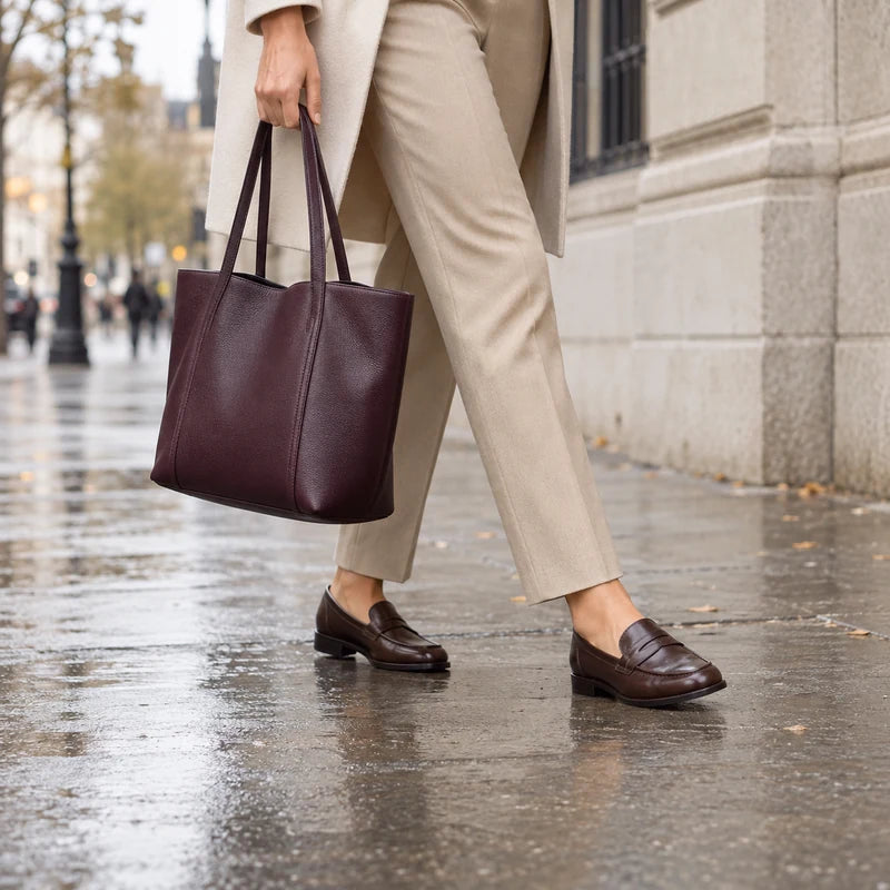 A commuter wearing leather loafers and carrying a leather tote on a damp city sidewalk