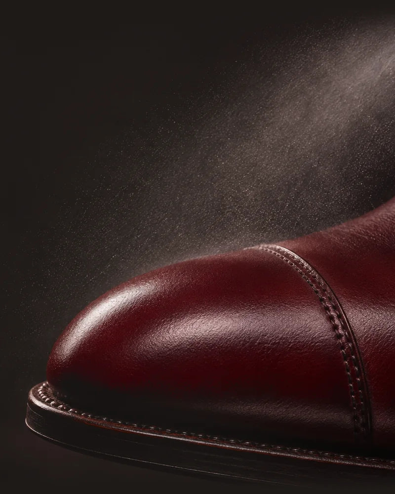 Illustration of a fine mist drifting over an oxblood cap-toe shoe on a dark background