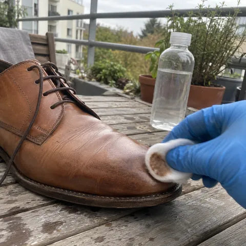 Illustrated step: wiping the toe of a tan leather shoe with a cotton pad before painting